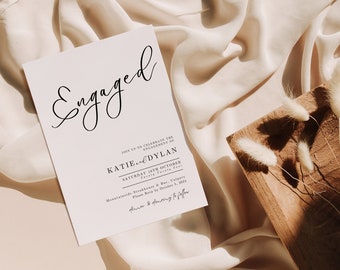 May include: A white card with black text announcing the engagement of Katie and Dylan. The card includes the date and location of the celebration, "Saturday 16th October, Mountainside Steakhouse & Bar, Calgary".