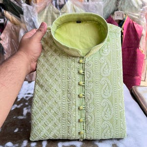 May include: A light green embroidered kurta with a white pattern and a row of yellow buttons down the front.