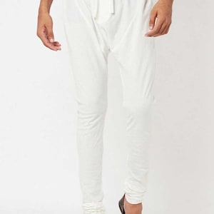 May include: White drawstring pants with a relaxed fit. The pants have a comfortable, loose design, with a drawstring at the waist. The bottom of the pants are gathered at the ankles. The pants are paired with dark brown shoes.