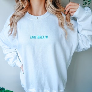May include: White sweatshirt with the text "TAKE BREATH" in blue lettering.