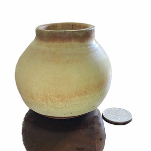 May include: A small, round, ceramic vase with a light green glaze and a brown rim. The vase is about the size of a quarter.