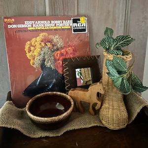 May include: A vintage vinyl record album with a brown and orange cover featuring a bouquet of flowers. The album title is "Eddy Arnold Bobby Bare Don Gibson Hank Snow Porter Wagoner Sing Popular Country Songs" with the RCA Victor logo. The album cover also features a sticker that says "The RCA Experience".