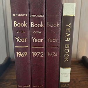 May include: A set of four burgundy leather-bound books titled "Book of the Year" with gold lettering. The books are from 1969, 1972, 1974, and 1982.