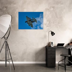 May include: A framed print of an airplane in flight against a blue sky with clouds. The biplane has the text "ARMEE DE L'AIR" on its wings. The print is displayed on a gray wall above a black desk with a lamp and a laptop.