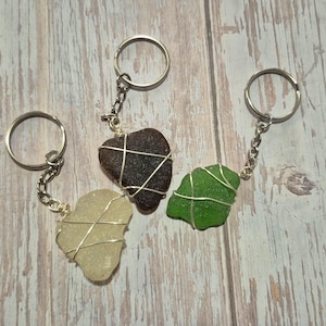 May include: Three keychains with different colored sea glass hearts. Each heart is wrapped in silver wire and attached to a silver key ring.