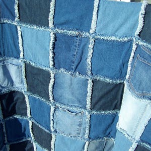May include: A patchwork quilt constructed from various shades of blue denim fabric squares. The quilt features a frayed seam design between each square, with several integrated denim pockets visible across the surface of the textile piece.