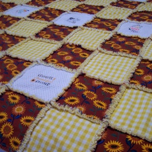 Op de afbeelding: Een patchworkdeken met een geel en wit ruitjespatroon, een rood en bruin zonnebloempatroon en witte stof met de tekst "Grateful Thankful Blessed".