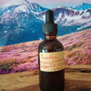 May include: A brown glass bottle with a black dropper top. The bottle is labeled "Feverfew Migraine Preventative" and "Dropper Full 1-3 Times a Day".