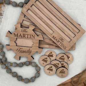 May include: Wooden family name puzzle with the name "The Martins" engraved on the top. The puzzle includes a jigsaw piece with "The Martin Family" and wooden train tokens numbered 3, 5, 6, and 8. A decorative wooden bead garland is also present.
