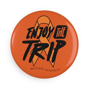 May include: Orange button with a black ribbon and the text "Enjoy the Trip" and the words "Multiple Sclerosis" at the bottom.