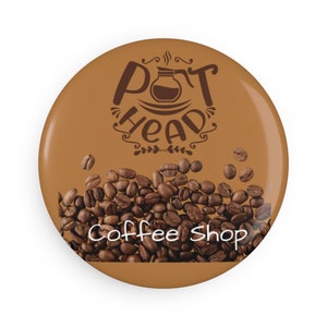 May include: A brown button with the text "Pot Head Coffee Shop" in white. The button features a stylized coffee pot with steam coming out of the spout and a pile of coffee beans.