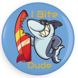 May include: A blue button featuring a cartoon shark wearing sunglasses and holding a red surfboard. The text "I Bite Dude" is written in yellow on the button.