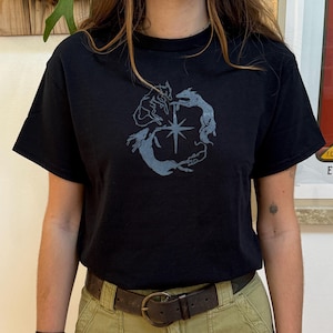 May include: A black t-shirt featuring a graphic design of four stylised dogs in a circle around a star. The dogs are in a light blue colour.