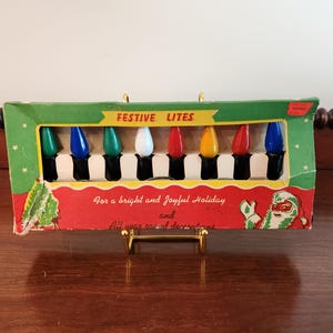 May include: A rectangular cardboard box containing eight colorful light bulbs in green, blue, white, red, and yellow. The packaging features the text FESTIVE LITES, For a bright and Joyful Holiday and All year round decorations, and a Santa illustration.