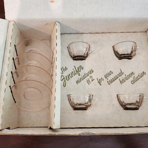 May include: A set of miniature pink glass teacups and saucers in a cardboard box. The box is labeled "The Jennifer miniatures #2 for your treasured heirloom collection."