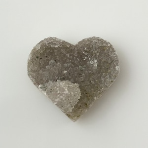 May include: A heart-shaped piece of gray and white crystal with a rough, textured surface.