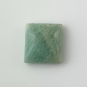 May include: A smooth, rectangular, light green amazonite gemstone with white streaks and swirls.