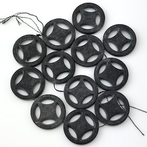 May include: A collection of dark gray, circular beads with a star-shaped design in the center. Each bead has a wheel-like appearance with four openings. The beads are strung together with black string, and are displayed on a white background.