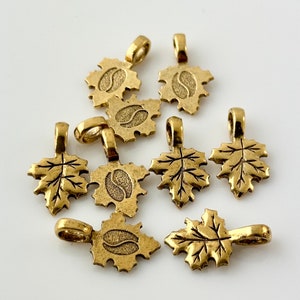 May include: Eight gold-tone metal leaf charms with a textured surface. Each charm has a loop at the top for attaching to jewelry or other crafts.