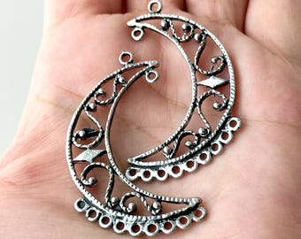 May include: Two silver crescent moon charms with intricate filigree designs. The charms have a beaded edge and a loop at the top for attaching to jewelry.