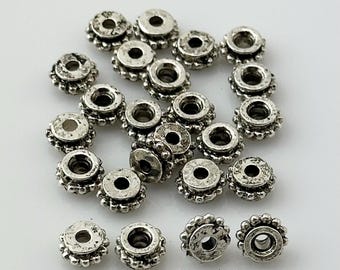 May include: A group of silver-toned metal spacer beads with a decorative design. The beads have a round shape with a small hole in the center.