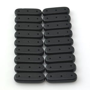 May include: A collection of twenty-one black, oval-shaped beads. Each bead has three evenly spaced holes. The beads are arranged in a grid pattern against a white background. These beads are likely used for jewelry making or crafts.