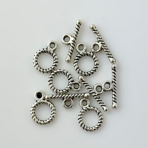 May include: A collection of silver-toned toggle clasps. The clasps feature a circular ring with a twisted rope design and a straight bar with a similar texture. The clasps are designed for jewelry making and crafting.