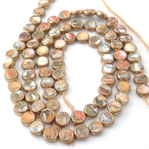 May include: A strand of round, gold-toned beads with a marbled pattern in shades of brown, orange, and white.