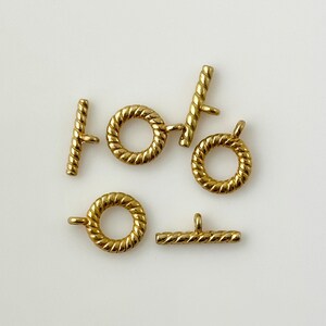 May include: A set of six gold-toned metal toggle clasps with a rope-like design. The clasps are in various shapes, including circles and bars.