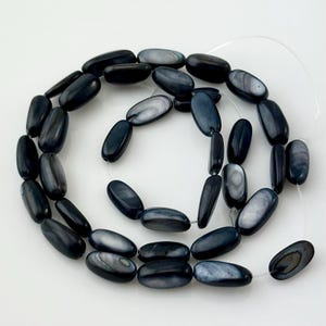 May include: A strand of oval-shaped black and white shell beads. The beads have a smooth, polished finish and are strung on a clear elastic cord.