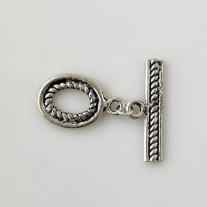 May include: Silver-toned toggle clasp with a rope-like design. The clasp has an oval loop and a straight bar with a chain connecting the two pieces.