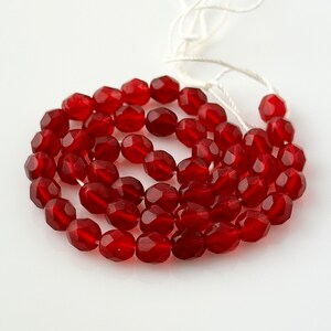 May include: A strand of red faceted glass beads. The beads are oval shaped and have a glossy finish.