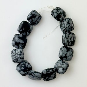 May include: A strand of black and white snowflake obsidian beads, each bead is square shaped and has a unique pattern.