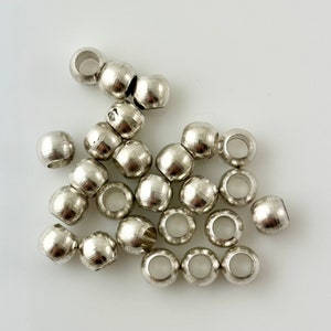 May include: A group of silver metal beads with a hole in the center of each bead. The beads are scattered on a white surface.