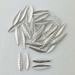 May include: A pile of silver-toned metal leaf-shaped charms. The charms are about 2 inches long and have a detailed design.