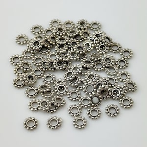 May include: A pile of silver-toned metal bead caps with a decorative, scalloped edge. The bead caps are small and round, with a hole in the center for threading.