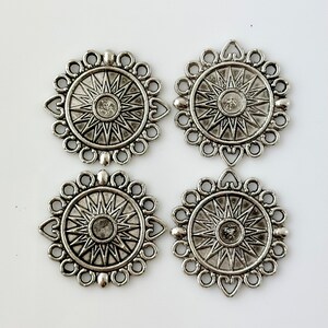 May include: Four silver-toned metal charms with a starburst design and a decorative border. Each charm has a hole for attaching to a necklace or bracelet.
