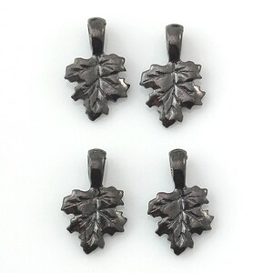 May include: Four dark gray leaf-shaped pendants with a loop at the top for attaching to a chain or cord. The pendants have detailed veining and a textured surface, perfect for jewelry making or crafting projects.