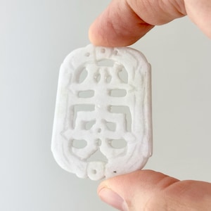 May include: White jade pendant carved with a Chinese character. The pendant is intricately detailed and has a smooth, polished finish.