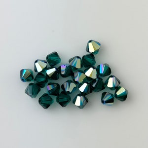 May include: A group of dark green faceted glass beads with iridescent accents. The beads are shaped like cones and are scattered on a white surface.