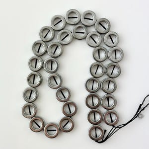 May include: Arrangement of silver metal eyelets with black thread, forming a curved shape. The eyelets are evenly spaced and have a dark line across the center. The background is plain white.