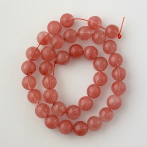 May include: A strand of pink and white gemstone beads. The beads are round and have a smooth, polished finish.