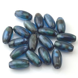 May include: A collection of oval-shaped beads with a dark blue and teal iridescent finish. The beads are scattered on a white surface, showcasing their glossy texture and color variations. These beads are suitable for jewelry making.