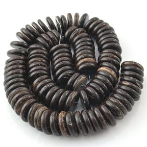 May include: A coiled strand of dark brown, disc-shaped beads with a smooth, polished finish. Each bead features a central hole and a slightly irregular, natural texture, arranged in a circular pattern on a plain white background.