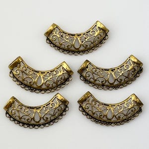 May include: Five gold-toned metal bead caps with a decorative filigree design. The caps are shaped like a half-circle and have a chain-like border.