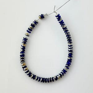 May include: A strand of blue and silver glass beads with gold accents. The beads are strung on a wire and are ready to be made into a necklace or bracelet.