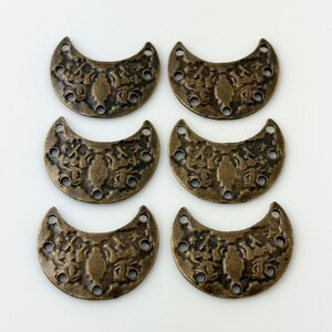 May include: Six antique gold-toned metal crescent moon charms with intricate designs and five holes each.