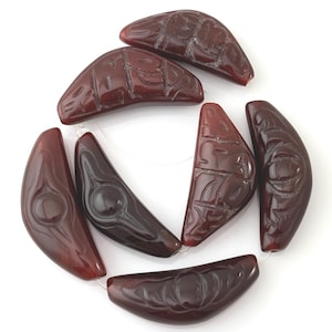 May include: A collection of dark red, crescent-shaped beads with carved designs. The beads are strung together, showcasing intricate patterns and a glossy finish. The shapes vary slightly, adding to their unique appeal.