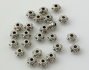 May include: A scattering of silver-toned metal beads with a decorative, raised, circular design. The beads have a small hole in the center for stringing.