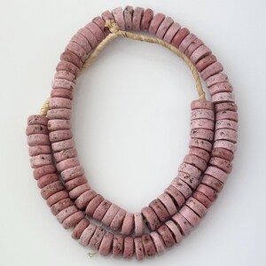 May include: A strand of pink and white speckled ceramic beads. The beads are round and have a slightly rough texture.
